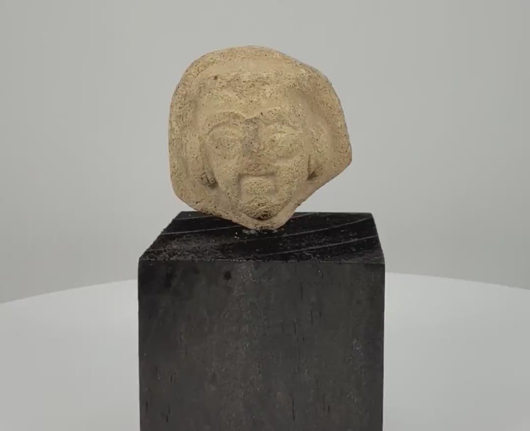 360-degree rotating video of an ancient Near Eastern terracotta male head fragment featuring a detailed beard, prominent facial features, deeply carved eyes, and a distinctive sculpted hairstyle. Dating to circa 1st millennium BCE, mounted on a black display stand.