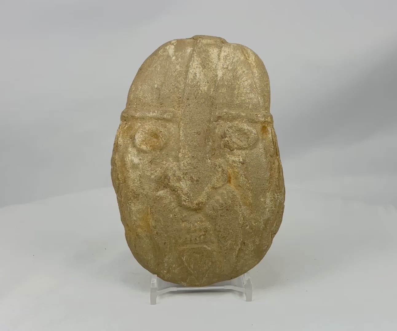 360-view of carved stone warrior effigy head showcasing helmet design, recessed eyes, textured surface, and primitive sculptural details