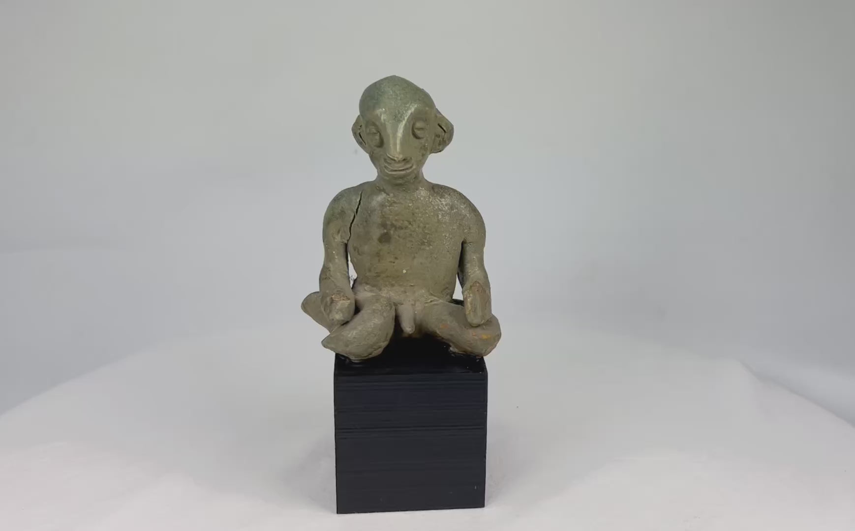 Hand-modeled West Mexican Nayarit Chinesco terracotta figure of a seated male with slit eyes, pinched nose, cross-legged pose, and red/orange pigment remnants, featuring earthen and mineral accretions, mounted on a modern wood display block, ca. 100 BCE–300 CE.