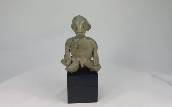 Hand-modeled West Mexican Nayarit Chinesco terracotta figure of a seated male with slit eyes, pinched nose, cross-legged pose, and red/orange pigment remnants, featuring earthen and mineral accretions, mounted on a modern wood display block, ca. 100 BCE–300 CE.