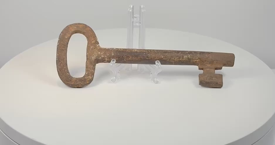 Rotating 360-degree view of an 18th-century European forged iron skeleton key, showing its oval bow, thick shaft, wedge-shaped ward, and aged patina.