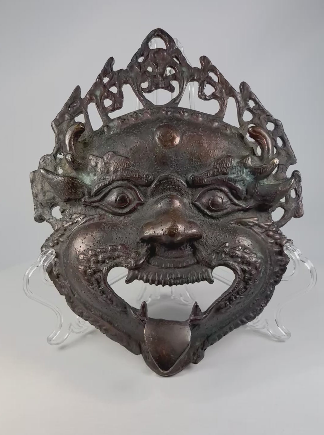 Late 19th–early 20th century Himalayan bronze or brass ritual mask, depicting fierce protective deity with wide eyes and grimacing mouth, traces of pigment, patina, used in Buddhist or Hindu ceremonies