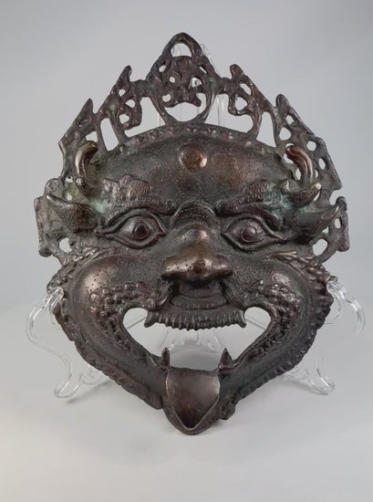 Late 19th–early 20th century Himalayan bronze or brass ritual mask, depicting fierce protective deity with wide eyes and grimacing mouth, traces of pigment, patina, used in Buddhist or Hindu ceremonies
