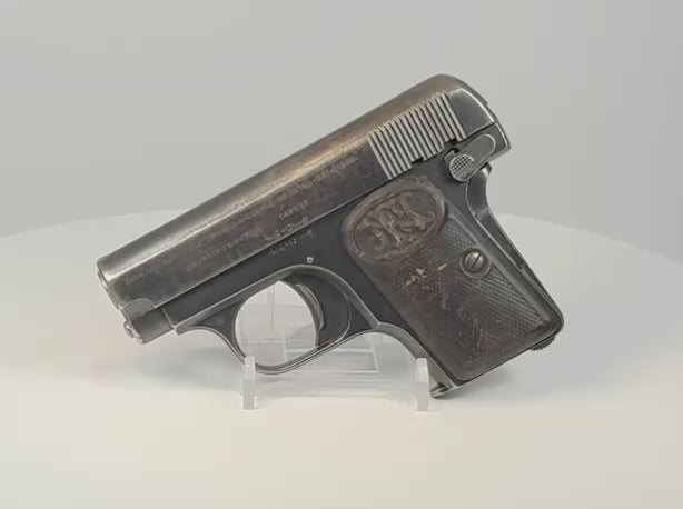 Deactivated FN Browning Model 1906 pocket pistol on a display stand, showing worn blued steel and checkered FN-monogram grips.