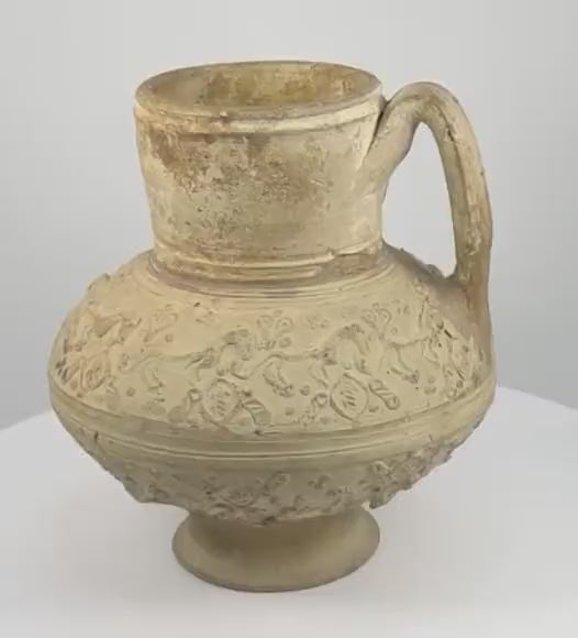 360-degree rotating view of a medieval Persian Seljuk-style pottery ewer, attributed to the 12th–13th century CE, featuring raised horse-like animal figures, heart-shaped ornamental motifs, decorative medallions, a rounded body, flared neck, curved handle, and aged buff-coloured earthenware surface.
