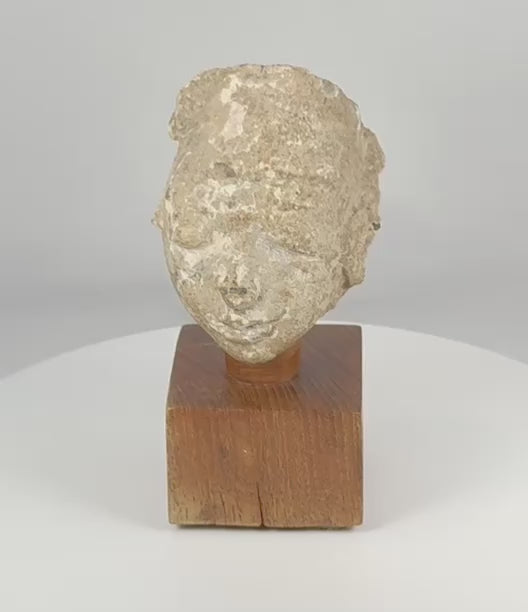 360-degree rotating view of an ancient Gandharan Buddhist stucco head fragment mounted on a wooden display base, showcasing its serene facial features, archaeological weathering, mineral deposits, and distinctive Kushan-period artistic style.