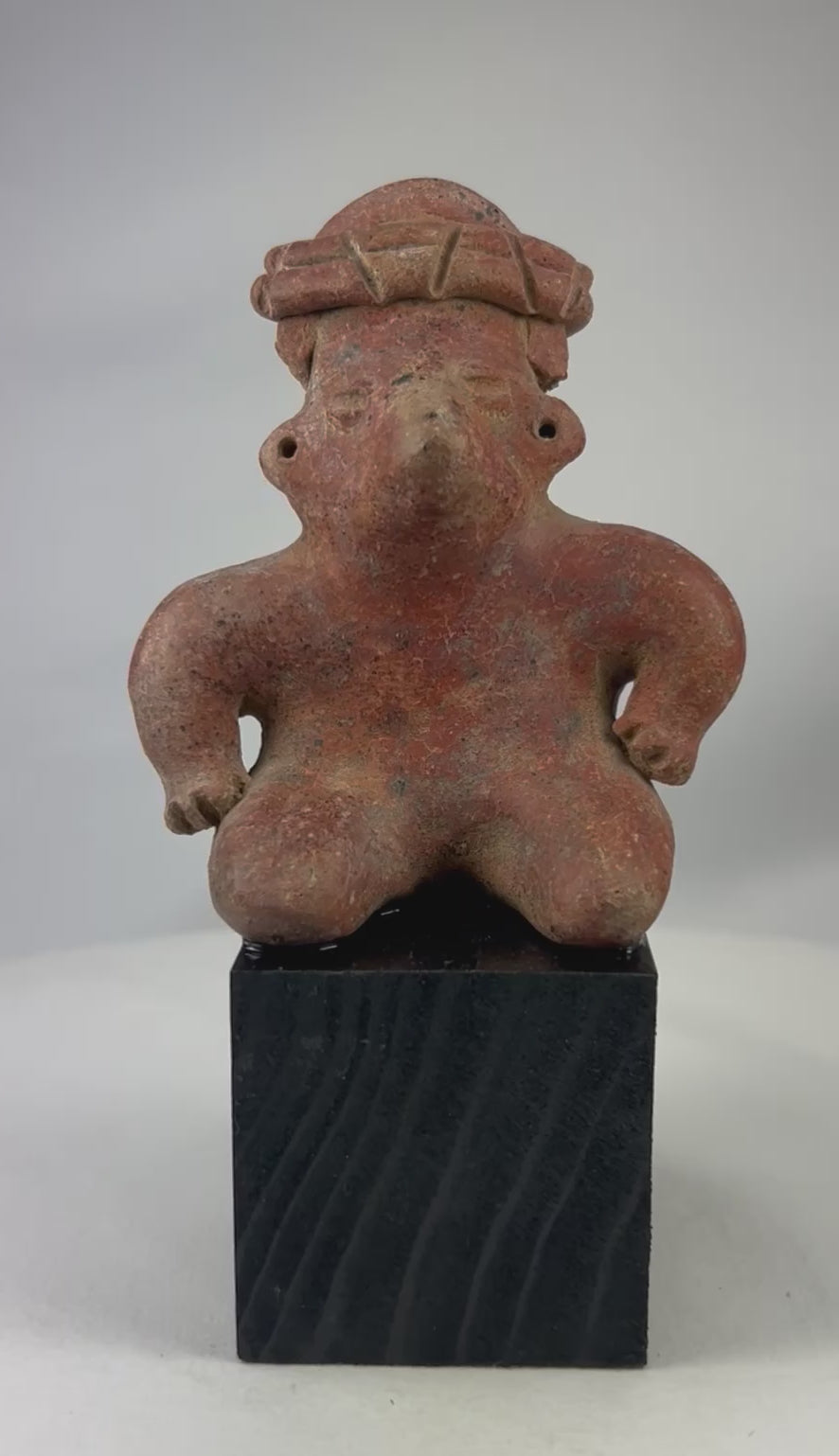 Rotating showcase video of Pre-Columbian West Mexico terracotta figure featuring stylized kneeling posture, headdress, pierced ears, and original red slip, circa 300 BCE–300 CE.