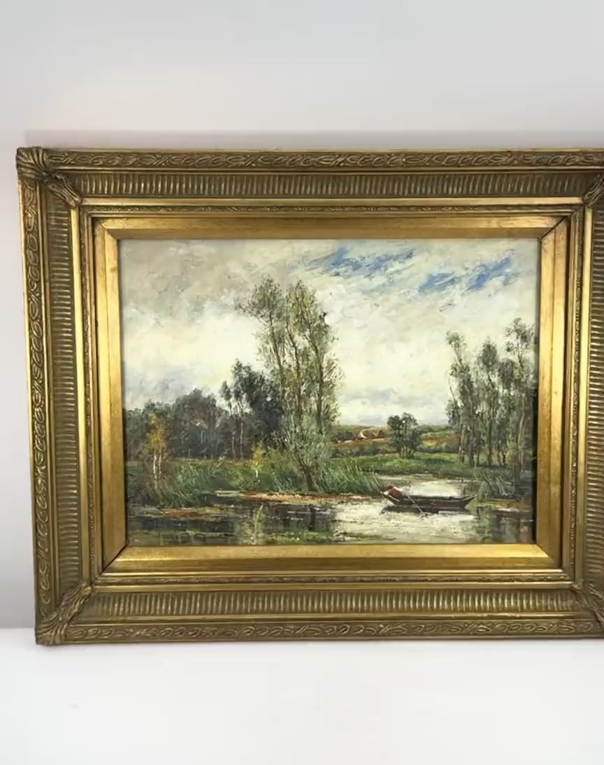 Antique early 20th-century Impressionist-style oil painting depicting a peaceful European river landscape with a solitary figure rowing a wooden boat, tall trees, lush greenery, and reflective water beneath a blue, cloud-filled sky. Presented in an ornate gilt frame with decorative foliate detailing.
