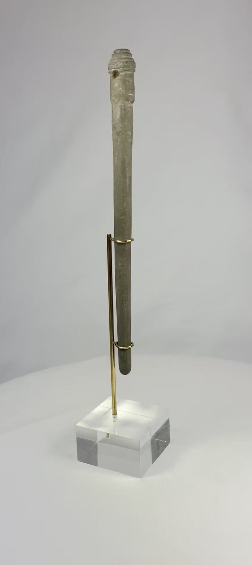 Video of an ancient Bactrian stone idol with Janus-style human head, elongated form, and smooth patina, displayed upright on a modern stand.