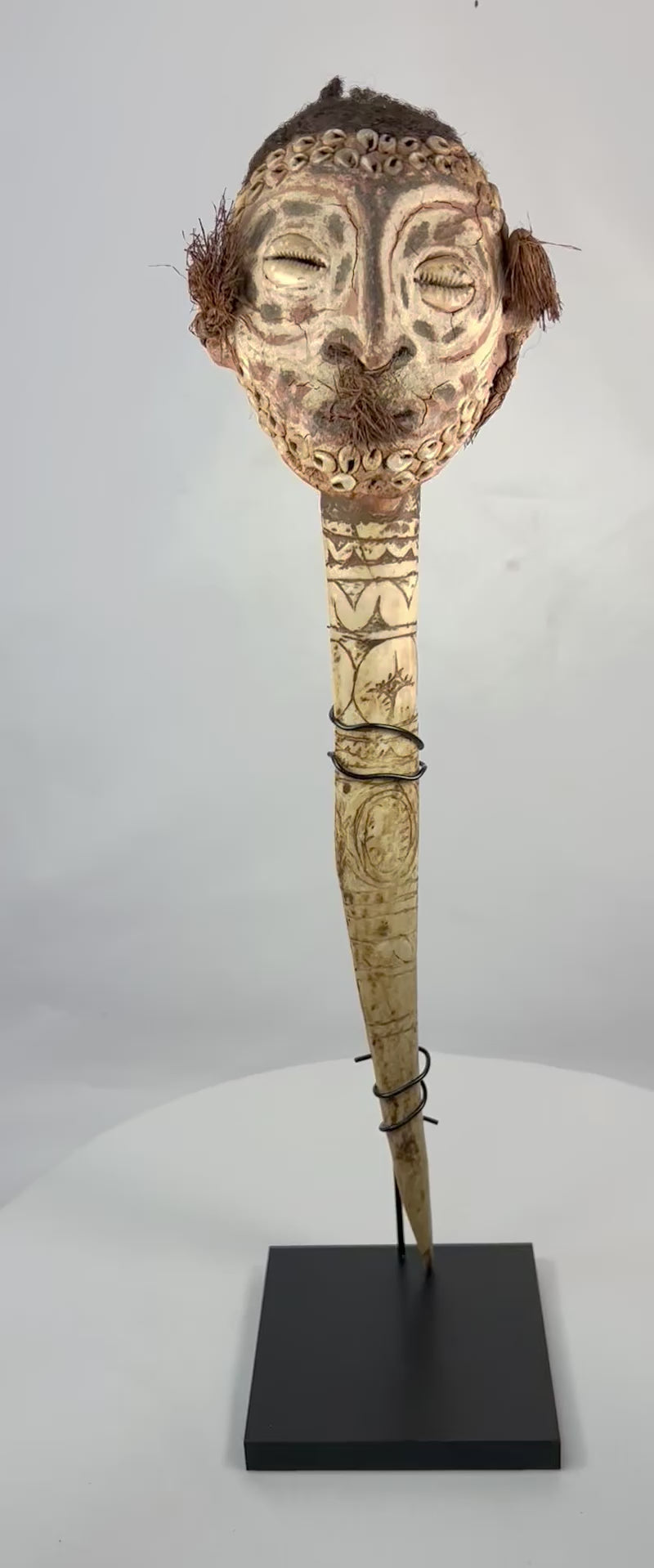 19th-century Sepik River ceremonial bone dagger with carved ancestral head, cowrie shell inlays, human hair adornments, and tribal geometric motifs, used in ritual and initiation rites.