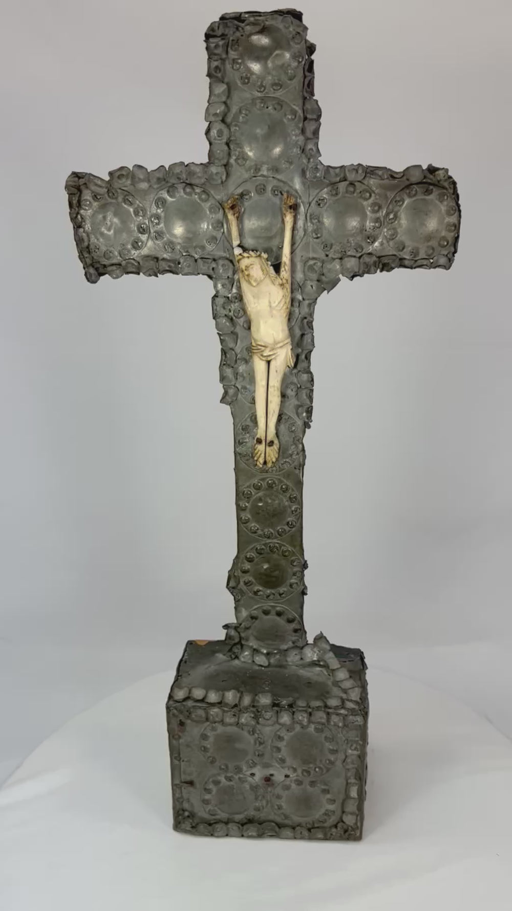 360° view of an antique hand-carved crucifix featuring a bone corpus on a repoussé-decorated wooden cross with aged patina, displayed under soft lighting on a white background.