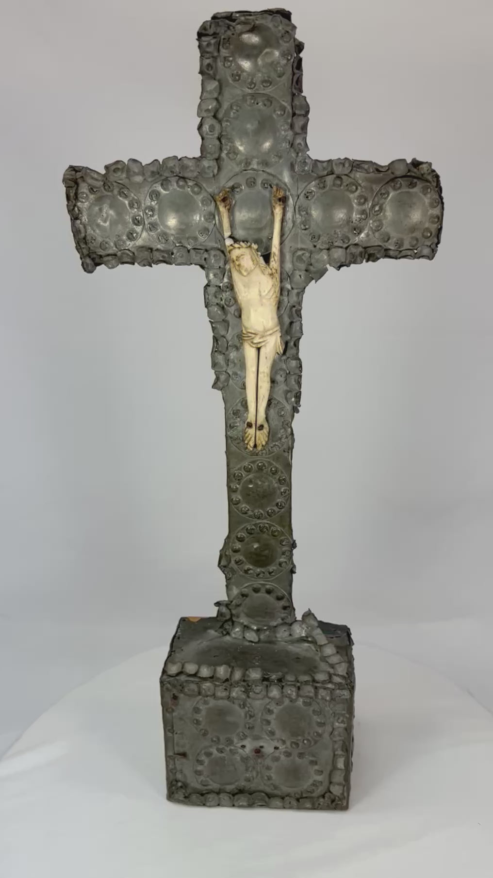 360° view of an antique hand-carved crucifix featuring a bone corpus on a repoussé-decorated wooden cross with aged patina, displayed under soft lighting on a white background.
