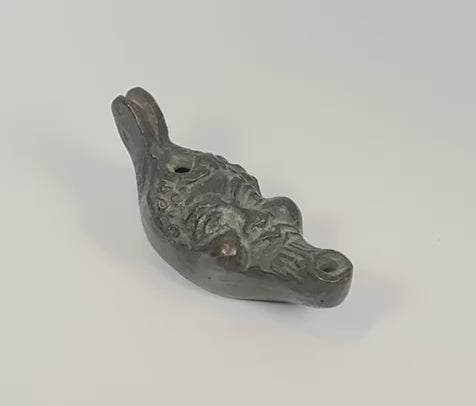 Rotating view of an antique grotesque satyr-form oil lamp featuring a cast metal mythological mask, filling aperture, wick nozzle, suspension holes, and dark aged patina, Europe, 19th century.