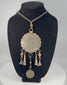 Rotating view of a mid-20th-century Central Asian tribal necklace with a large scalloped circular pendant, engraved six-petalled rosette, turquoise-coloured central cabochon, faceted orange beads, banded bead, conical and triangular metal drops, worn coin with Arabic or Persian script, interlinked metal chain, handmade suspension rings, tarnishing, oxidation, and aged patina