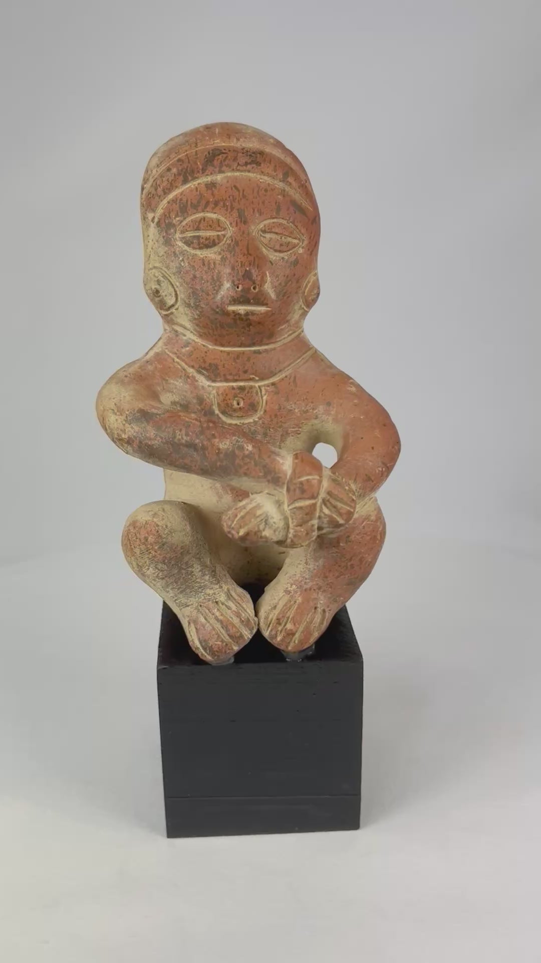 Pre-Columbian seated terracotta figure from West Mexico (Nayarit/Jalisco), circa 300 BCE–300 CE, hand-molded with red slip, stylized anthropomorphic features, burnished surface, shaft tomb funerary artifact on black display stand