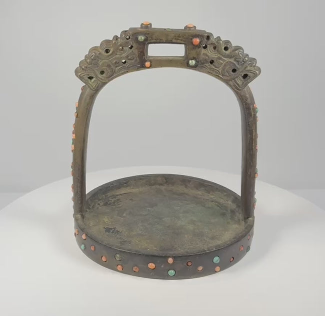 Rotating 360-degree video of an 18th–19th century Mongolian or Tibetan bronze stirrup, showing its dragon-head terminals, pierced latticework, coral and turquoise inlays, wide tread, saddle loop, and aged patina.