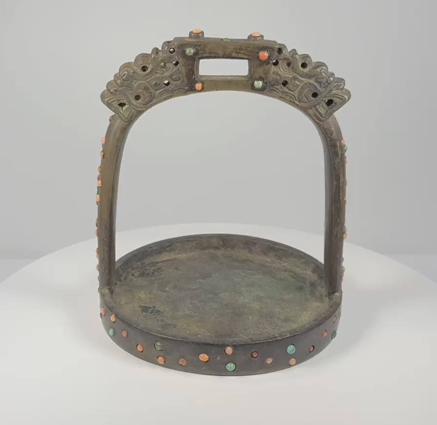 Rotating 360-degree video of an 18th–19th century Mongolian or Tibetan bronze stirrup, showing its dragon-head terminals, pierced latticework, coral and turquoise inlays, wide tread, saddle loop, and aged patina.