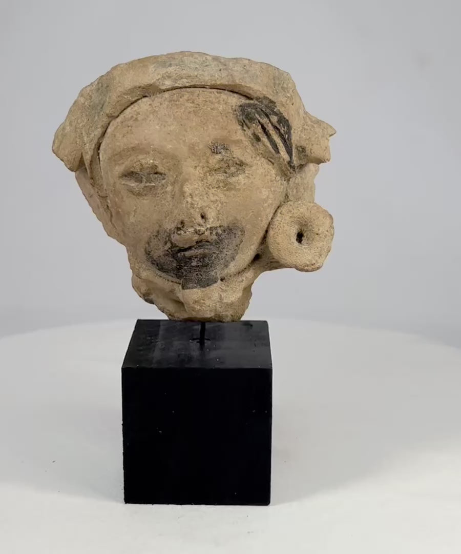 Late Classic Period Mesoamerican ceramic head fragment, circa 500–900 CE, with expressive facial features, traces of black pigment, and a detailed turban-like headpiece.
