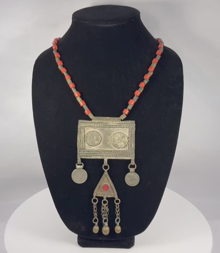 Antique Turkmen tribal necklace featuring a large rectangular pectoral pendant, triangular tumar amulet, silver-toned metal, red glass beads, suspended coin elements, and handcrafted Central Asian ceremonial craftsmanship dating to the late 19th or early 20th century.
