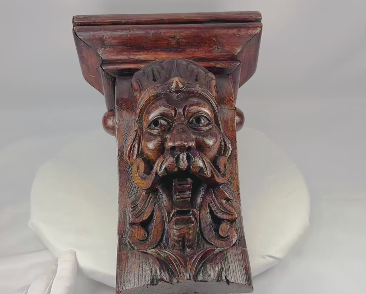Antique 19th-century European wooden corbel, hand-carved with a grotesque crowned face featuring a prominent mustache and ornamental details. Dark natural patina, Gothic-inspired design, and architectural functionality. Serves as both structural support and decorative element, reflecting historic woodcarving traditions and Gothic revival aesthetics.
