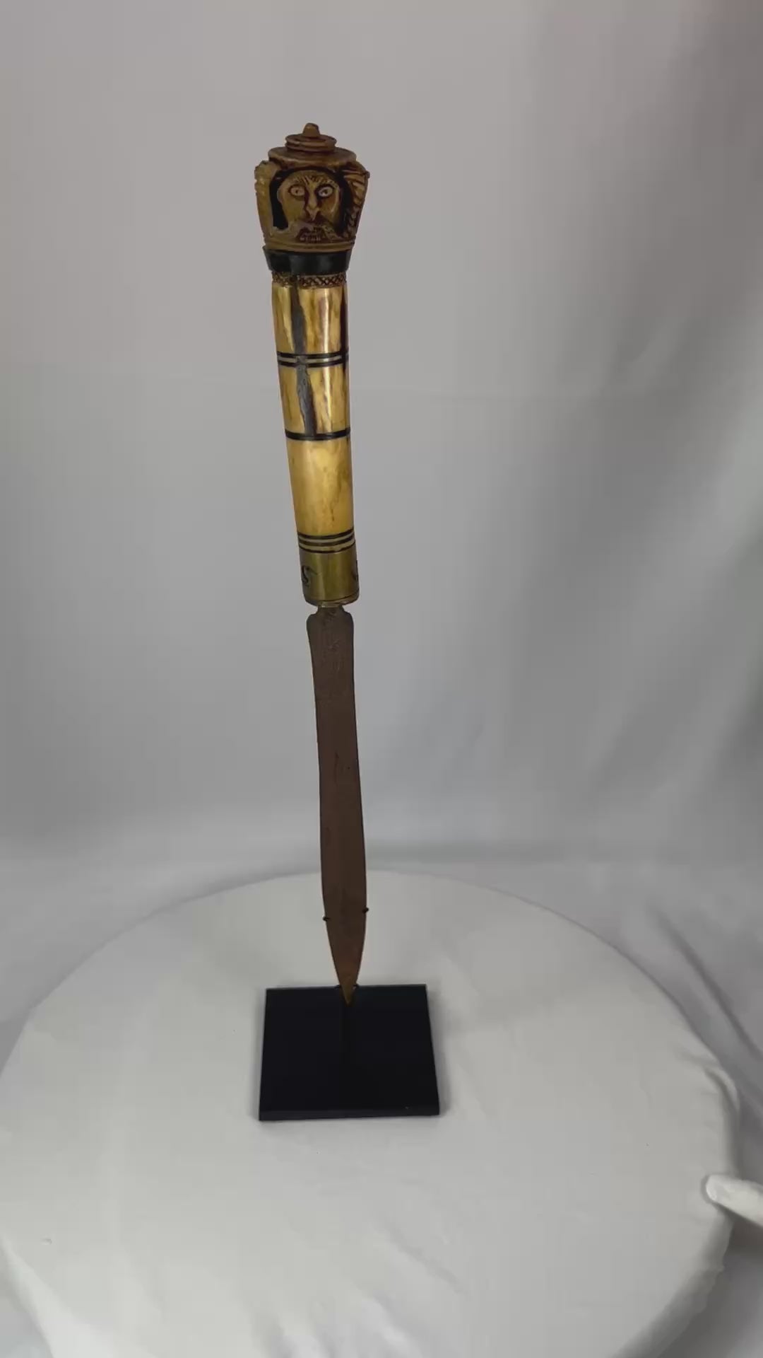 Indonesian Dayak knife from 19th century with carved bone handle depicting an Aso guardian beast and a male figure with elaborate mustache, steel blade, patinated surface, reflecting ritual and cultural significance of Borneo craftsmanship.