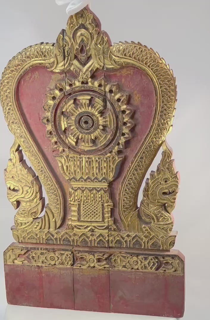 Thai Buddhist shrine panel carved from teakwood, gilded over red lacquer, featuring central dharmachakra and twin naga serpents, late 19th century, Rattanakosin/Lanna tradition, 24.5 x 15 inches