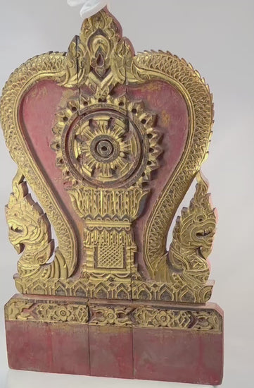 Thai Buddhist shrine panel carved from teakwood, gilded over red lacquer, featuring central dharmachakra and twin naga serpents, late 19th century, Rattanakosin/Lanna tradition, 24.5 x 15 inches