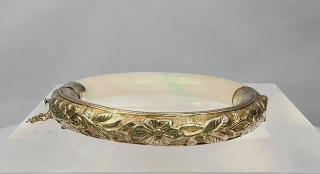 Rotating view of an antique Chinese hinged jade or hardstone bracelet with pale celadon colouring, natural green inclusions, repoussé floral silver mounts, a safety chain, and an interior SILVER mark