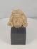Rotating view of a Pre-Columbian carved stone head fragment with recessed eyes, a triangular nose, circular earspools, an elaborate headdress, weathered surfaces, and a custom display stand
