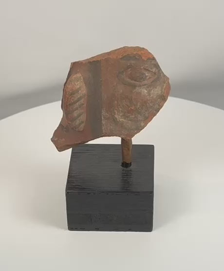 Rotating view of an ancient terracotta figural fragment showing a stylized face, painted ear ornament, surviving pigment traces, and archaeological surface details from multiple angles.