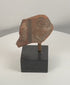 Rotating view of an ancient terracotta figural fragment showing a stylized face, painted ear ornament, surviving pigment traces, and archaeological surface details from multiple angles.