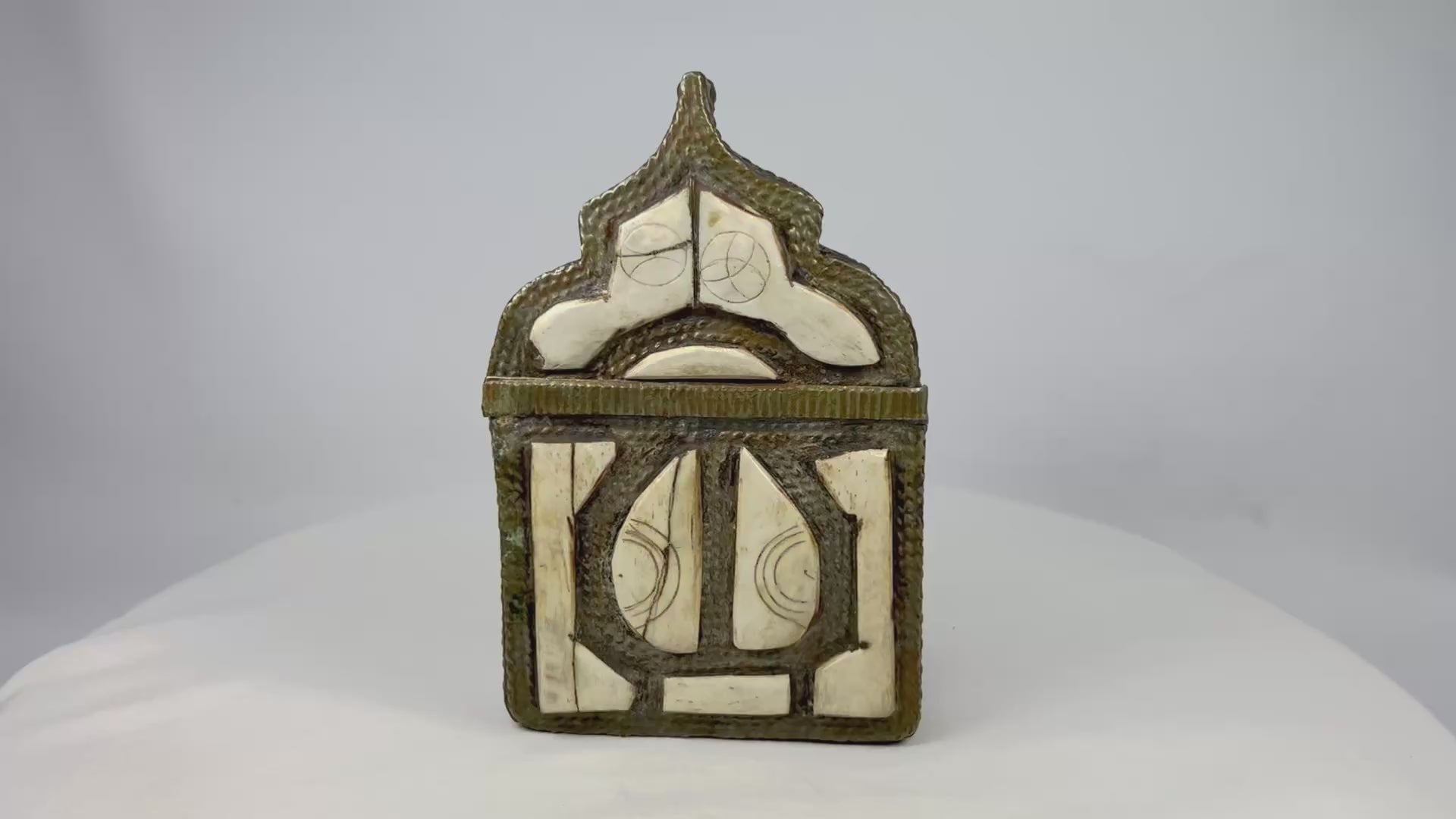 Ornate 19th-century Moroccan Berber amulet box with hinged pointed-arch lid, hammered brass body, carved bone inlay with geometric designs, and rich patina, used to house protective talismans and Quranic verses