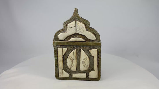 Ornate 19th-century Moroccan Berber amulet box with hinged pointed-arch lid, hammered brass body, carved bone inlay with geometric designs, and rich patina, used to house protective talismans and Quranic verses