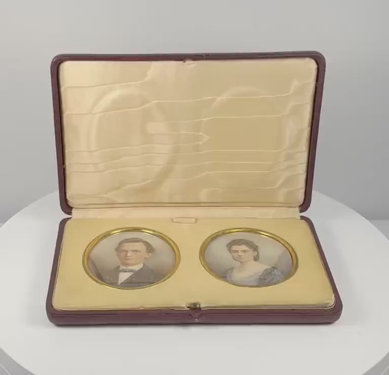 360-degree rotating view of a matched pair of late Victorian to Edwardian colour portrait miniatures, circa 1880–1910 CE, depicting a formally dressed gentleman and woman. Both oval portraits feature gilt-coloured metal surrounds and are displayed in a burgundy leather-covered presentation case with cream velvet mounting, satin lining, and folding easel support. Formerly part of the historic Sears family collection from the estate of Joseph W. Haley, Pride's Crossing, Massachusetts, USA.