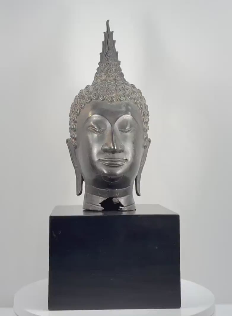 360-degree rotating view of a large 18-inch Thai bronze Buddha head attributed to the 19th-century Rattanakosin period, featuring Sukhothai-style spiral hair curls, a tall flame-shaped ushnisha, downcast eyes, elongated earlobes, a serene expression, dark metallic patina, and visible age-related wear and damage at the lower neck.