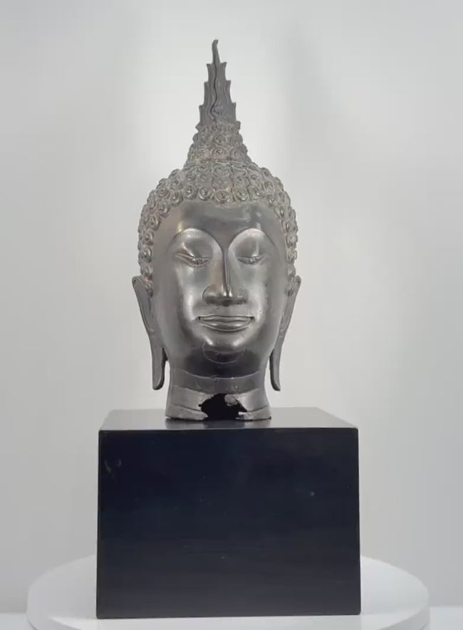 360-degree rotating view of a large 18-inch Thai bronze Buddha head attributed to the 19th-century Rattanakosin period, featuring Sukhothai-style spiral hair curls, a tall flame-shaped ushnisha, downcast eyes, elongated earlobes, a serene expression, dark metallic patina, and visible age-related wear and damage at the lower neck.