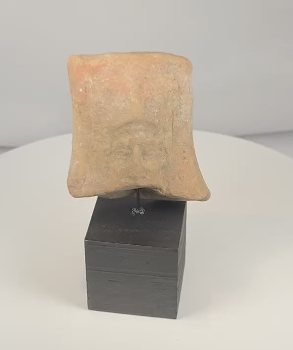 Rotating view of an ancient Hellenistic-Roman mold-made terracotta relief fragment depicting a mature male face with deeply set eyes, broad nose, moustache or short beard, raised border, red pigment traces, and a custom black display stand