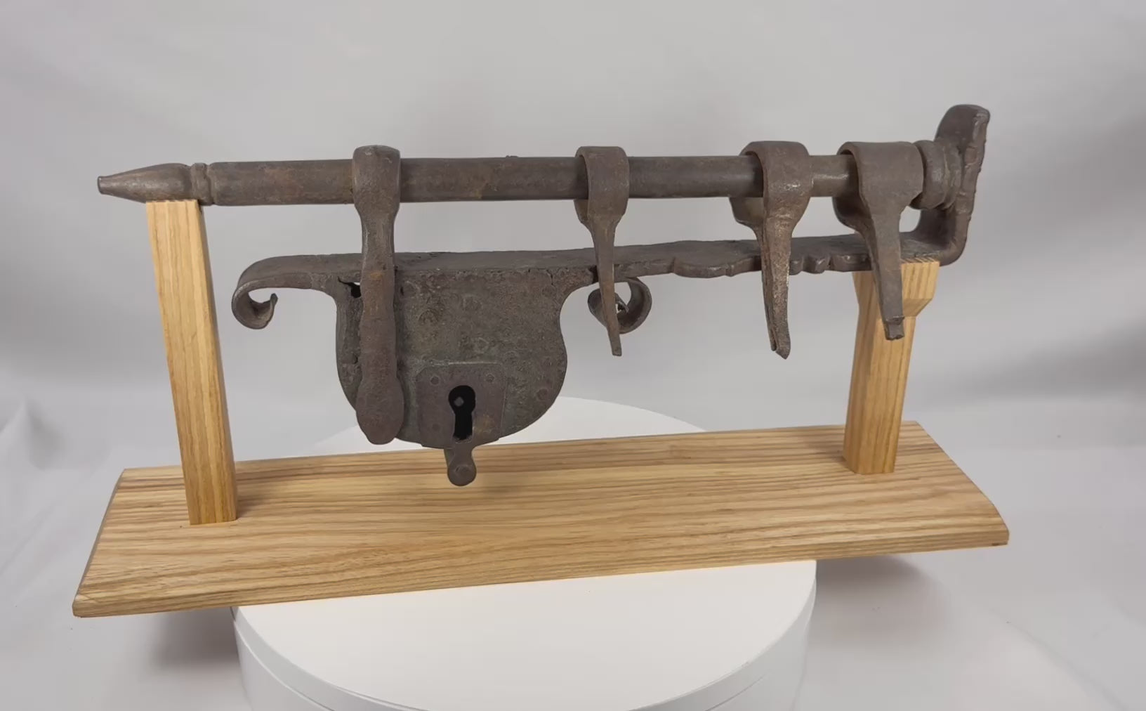 Rotating presentation of a large 18th-century European wrought-iron sliding hasp gate lock with riveted lock body and custom wooden stand