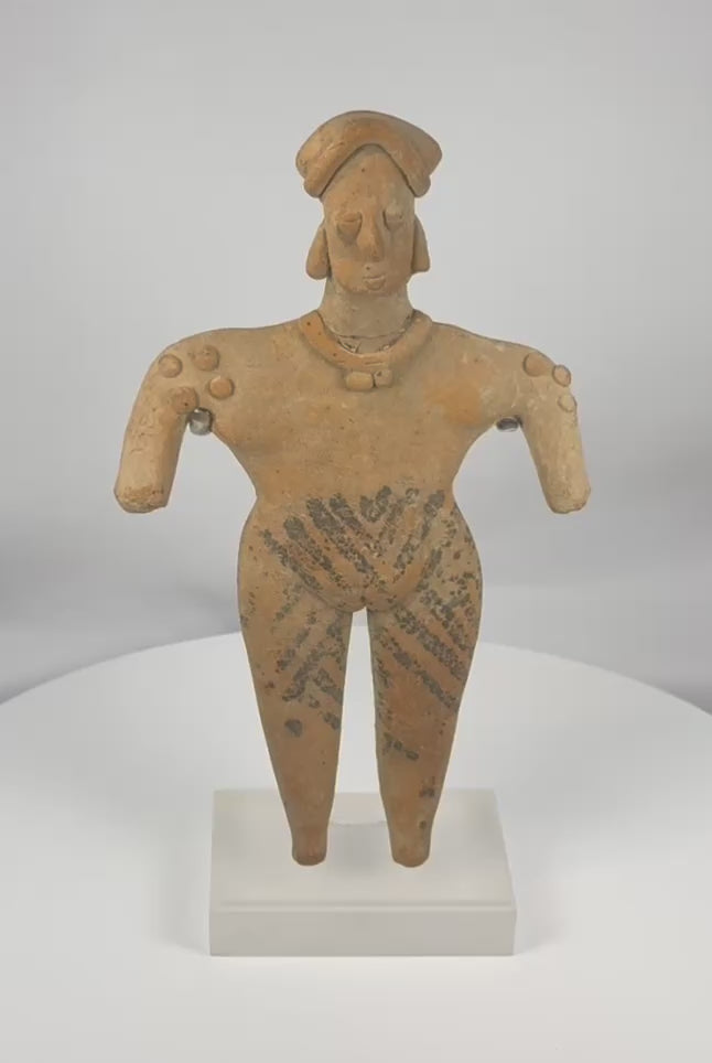 Ancient Colima terracotta female figure from West Mexico, dating to circa 300 BCE–300 CE, featuring black pigment decoration, an elaborate headdress, applied jewelry details, and mounted on a custom display stand. The video concludes with original 1985 Harmer Rooke Galleries provenance documentation and period collection photographs.