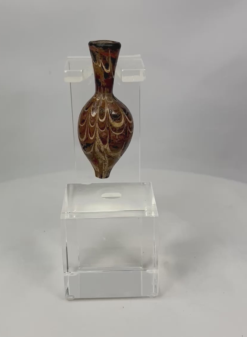 Ancient Eastern Mediterranean core-formed glass alabastron, 5th–6th Century AD, Late Roman to Byzantine period. Teardrop-shaped vessel with slender neck and pointed base, decorated with marbled browns, yellows, and gold, featuring delicate yellow trailing and swirling designs. Used for oils and perfumes, reflecting luxury, artistry, and status in antiquity.