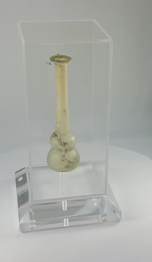 Ancient Roman clear glass double gourd balsamarium from the Eastern Mediterranean, 2nd–3rd Century CE. Features two globular sections joined by a slender neck, naturally iridescent patina, and substantial size for holding perfumes or balms. Reflects Roman glassmaking sophistication, luxury, and daily bathhouse culture.