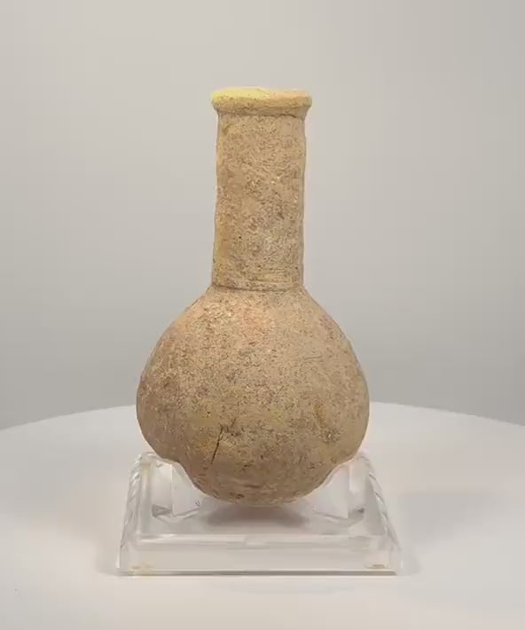 360-degree rotating view of an attributed Roman Imperial stone unguentarium, circa 1st–3rd century CE, featuring a rounded bulbous body, elongated cylindrical neck, thick flared rim, and weathered beige stone surface. The video highlights the vessel’s distinctive shape and porous texture.