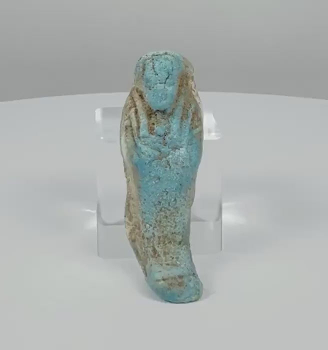 360-degree rotating view of an Ancient Egyptian turquoise-blue faience ushabti funerary figure, attributed to the Late Period–Ptolemaic Period (664–30 BCE), showing its mummiform body, crossed arms, stylized facial features, projecting foot base, and weathered blue glaze with earthy-brown deposits.