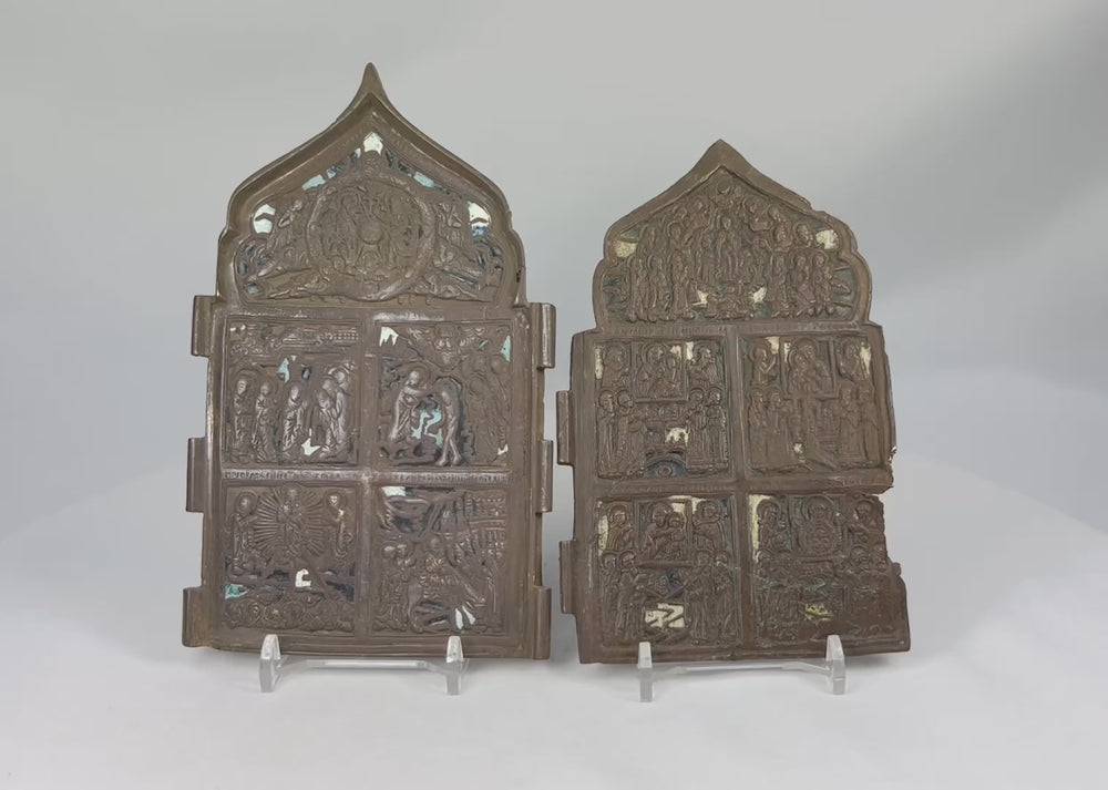 Rotating view of a matched pair of antique Russian Orthodox bronze traveling icons, showing detailed religious relief scenes, cathedral-arched tops, and beautiful aged patina.