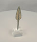 Rotating view of an ancient Western Asiatic bronze projectile point with an elongated lanceolate blade, pronounced raised central rib, long rectangular tang, rounded tip, green and blue-green patination, pale mineral encrustation, and a modern clear acrylic display base