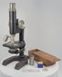 360-degree rotating view of an antique Spencer Lens Company compound monocular microscope, circa 1910–1920, featuring a black enamelled body, nickel-plated brass fittings, triple-objective nosepiece, precision focusing wheels, and horseshoe-shaped base. Accompanied by its original-style wooden carrying cabinet, glass slides, and scientific accessories.