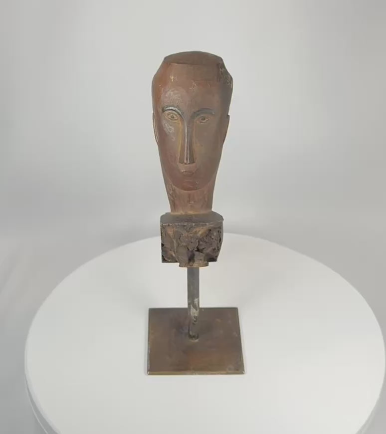 Rotating view of a Southeast Asian carved hardwood ceremonial figure fragment displaying expressive stylized facial features, weathered aged wood surface, traces of pigment, and mounted presentation on a custom metal display stand.