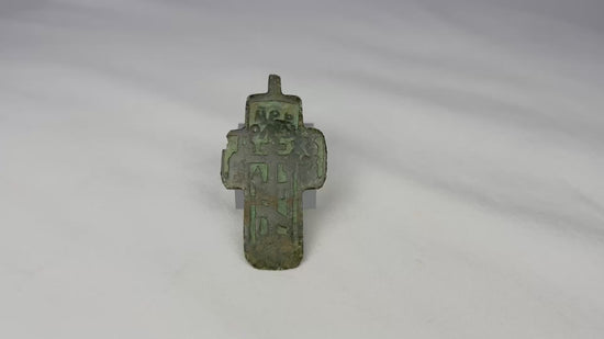 Small Russian Orthodox devotional cross-plaquette from the Old Believer tradition, cast in copper-alloy with champlevé green enamel remnants, blocky Cyrillic inscription panels, and deep olive patina, circa 1780–1820.