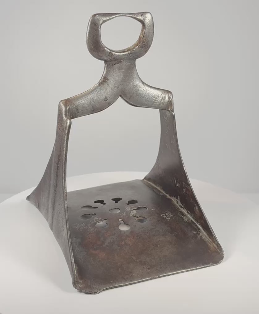 Rotating 360-degree video of a 17th-century Ottoman forged steel stirrup, showing its triangular frame, pierced floral footplate, broad saddle loop, silver damascening traces, and aged patina.