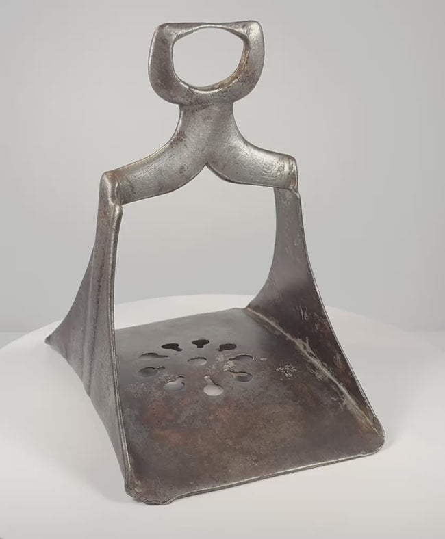 Rotating 360-degree video of a 17th-century Ottoman forged steel stirrup, showing its triangular frame, pierced floral footplate, broad saddle loop, silver damascening traces, and aged patina.